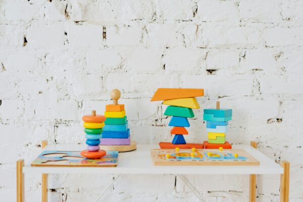 Colorful fine motor skills toys in Pakistan including stacking rings, wooden puzzles, and balance blocks on a white shelf against a brick wall