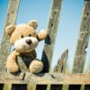 Teddy bear jumping over a wooden fence under the sky, symbolizing playful childhood moments with outdoor toys in Pakistan
